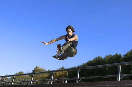 Active roller boy jumping from parapet on the blue skyの写真素材