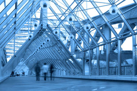 Blue glass corridor in bridge and people walkingの写真素材