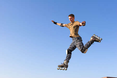 Active roller boy jumping from parapet on the blue skyの写真素材