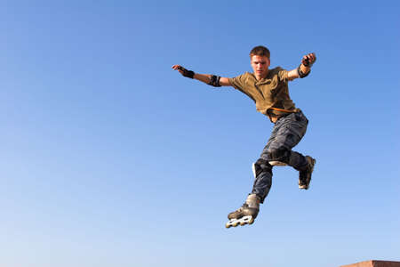 Active roller boy jumping from parapet on the blue skyの写真素材