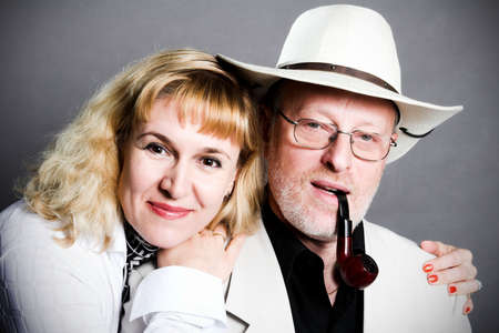 smiling adult couple in studio, man in hat and with tobacco pipeの写真素材