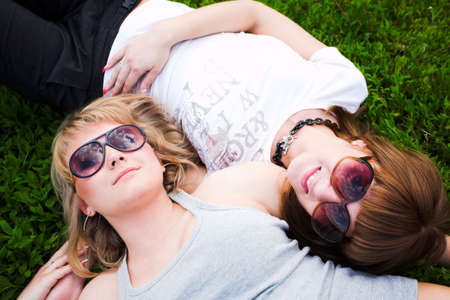 Two girls in sunglasses lay on green grass