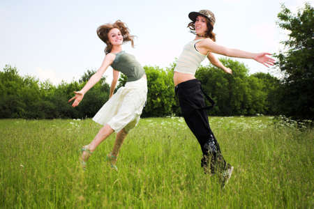 Two jumping girls on blue sky and green grassの写真素材