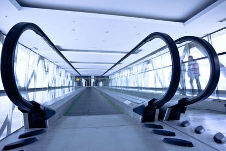 People move in grey corridor with escalators in office centre