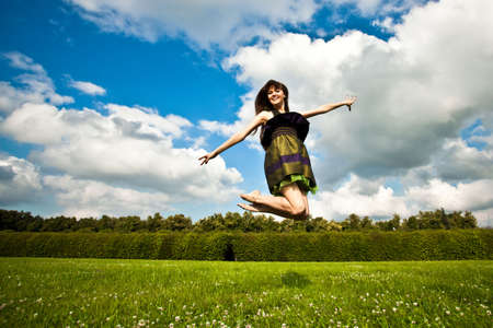 Pretty smiling girl with long brown hairs is jumping on green meadow