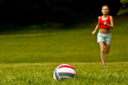 Girl run for volleyball ball lay on grassの写真素材