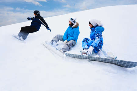 Snow splashes from board and two young girls sit on the bottom of the mountainの写真素材