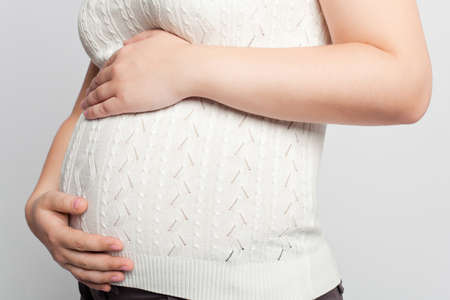 Pregnant woman in suit and jacket profile with hands on bellyの写真素材