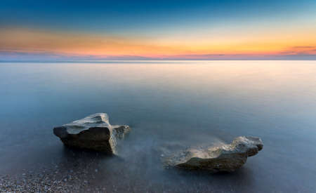 astonishing radiant sunset and tworocks in the silky waterの写真素材