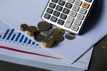 Many coins and calculator with chart paper as background on tableの写真素材