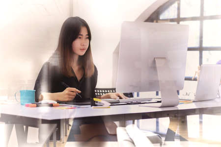 Young asian graphic designer working on computer using digital tablet at office.