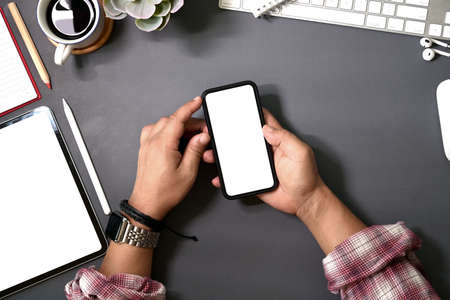 Top view man using a mobile smartphone over a workspace desk that has blank mockup screen.の写真素材