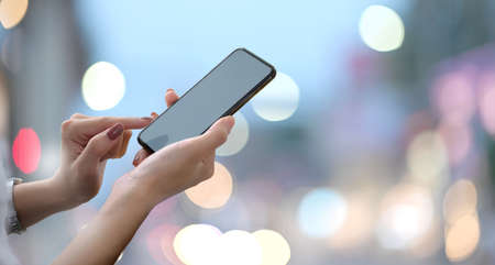 Female hands holding blank screen smartphone with blurred bokeh background.の写真素材