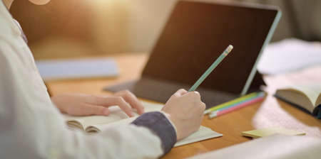 Close-up of young teenager girl working on her homework in school library room with blurred...