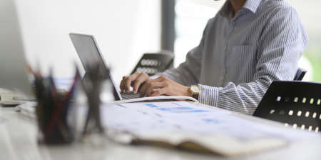 Young successful business man working in his modern office while typing on laptop computerの写真素材