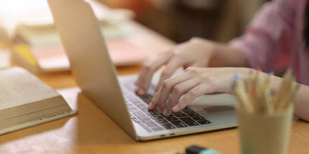 College girl typing her topics on laptop in library, close up viewの写真素材