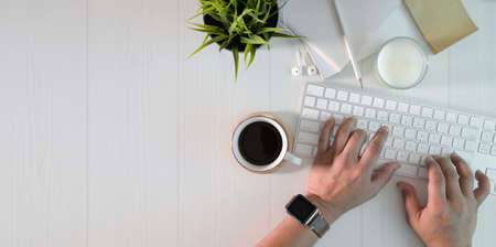 Top view of man typing on keyboard in minimal white work space with office suppliesの写真素材