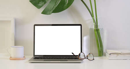 Freelancer's workspace with blank screen laptop on white wooden tableの写真素材