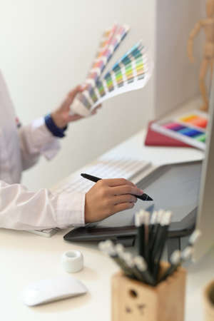 Close-up of female designer's hands drawing on her tablet in creative studio with blurred background