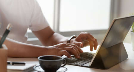 Close-up view of young man typing on keyboard laptop in minimal office roomの写真素材