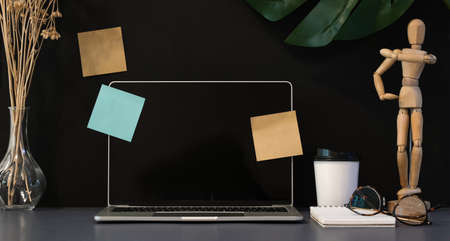 Stylish workplace with open laptop on grey desk and office decorations with dark wall backgroundの写真素材