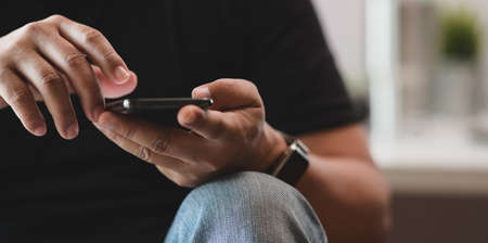 Young male touching his smartphone in his workplace with close up view and blurred backgroundの写真素材
