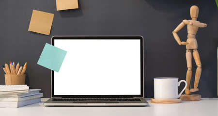 Open blank screen laptop in dark stylish work place with decorations and stationary on white tableの写真素材