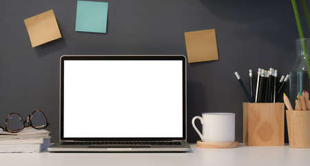 Freelancer's workplace with open blank screen laptop with dark background wall and office suppliesの写真素材