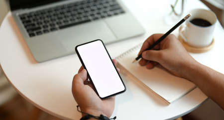 Freelancer writing his ideas on notebook while surfing the internet on smartphoneの写真素材