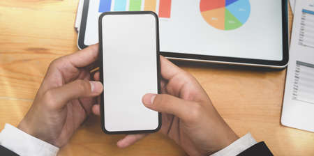 Businessman's hand holding blank screen smartphone in the meeting room while expressing the ideas with chartsの写真素材