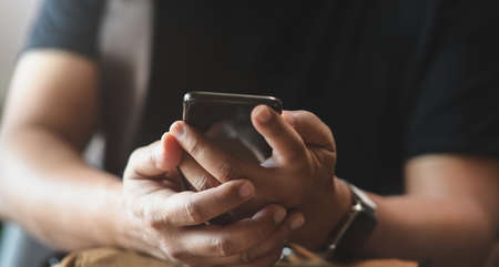 Close-up view of young man holding smartphone while carrying backpackの写真素材