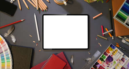 Overhead shot of artist's studio with blank screen tablet with painting tools and stationery on dark...