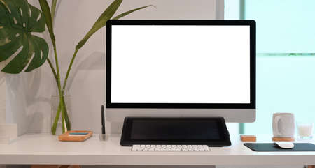 Relaxing work place with blank screen computer and office supplies on white wooden table in minimal office styleの写真素材