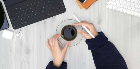 Top view of young female hands holding cup of coffee while working her projectの写真素材