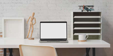 Simple white workplace with open blank screen laptop and office supplies with white brick wall backgroundの写真素材