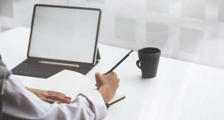 Close-up view of young businessman working on his plan with blank screen tablet while writing the idea on notebookの写真素材