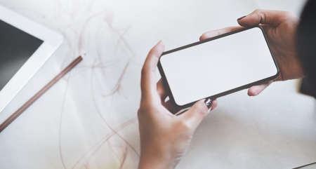 Close-up view of young man's hand holding blank screen smartphone in stylish office roomの写真素材
