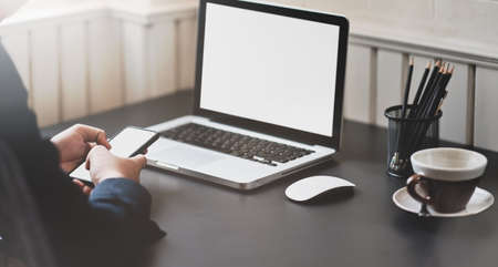 Businessman working on blank screen laptop while holding his smartphone in stylish workplaceの写真素材