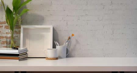 Modern workplace with mock up frame and copy space on white wooden table and white brick wall backgroundの写真素材