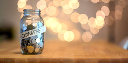 Jar full of coins for donation on wooden desk with blurred backgroundの写真素材