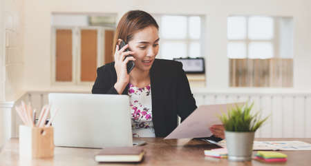 Businesswoman talking with customer on smartphone in officeの写真素材