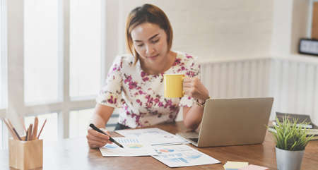 Beautiful businesswoman working on her project while drinking the coffee in comfortable officeの写真素材