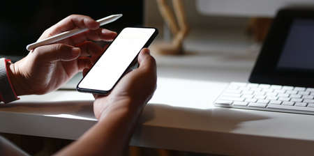Young male freelancer searching the ideas from blank screen smartphone in his comfortable workplaceの写真素材