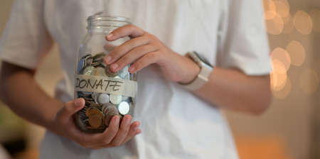 Cropped view of young girl holding a jar full of coins for donation with blurred backgroundの写真素材