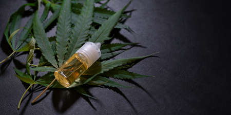 Close-up view of marijuana leaves and cannabis oil bottles for treatment on dark backgroundの写真素材