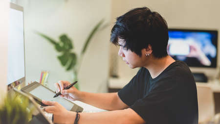 Young professional male photographer retouching his photos with digital tablet in comfortable workplaceの写真素材