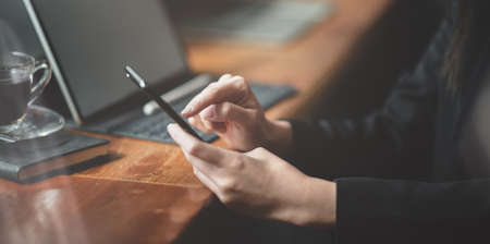 Cropped view of businesswoman working on tablet while using smartphone in modern office roomの写真素材