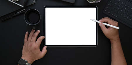 Overhead shot of man drawing on blank screen tablet in dark luxury office with copy space
