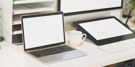 Comfortable workplace with blank screen laptop, coffee cup and office supplies