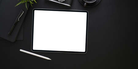 Top view of blank screen tablet and office supplies in dark stylish workplace